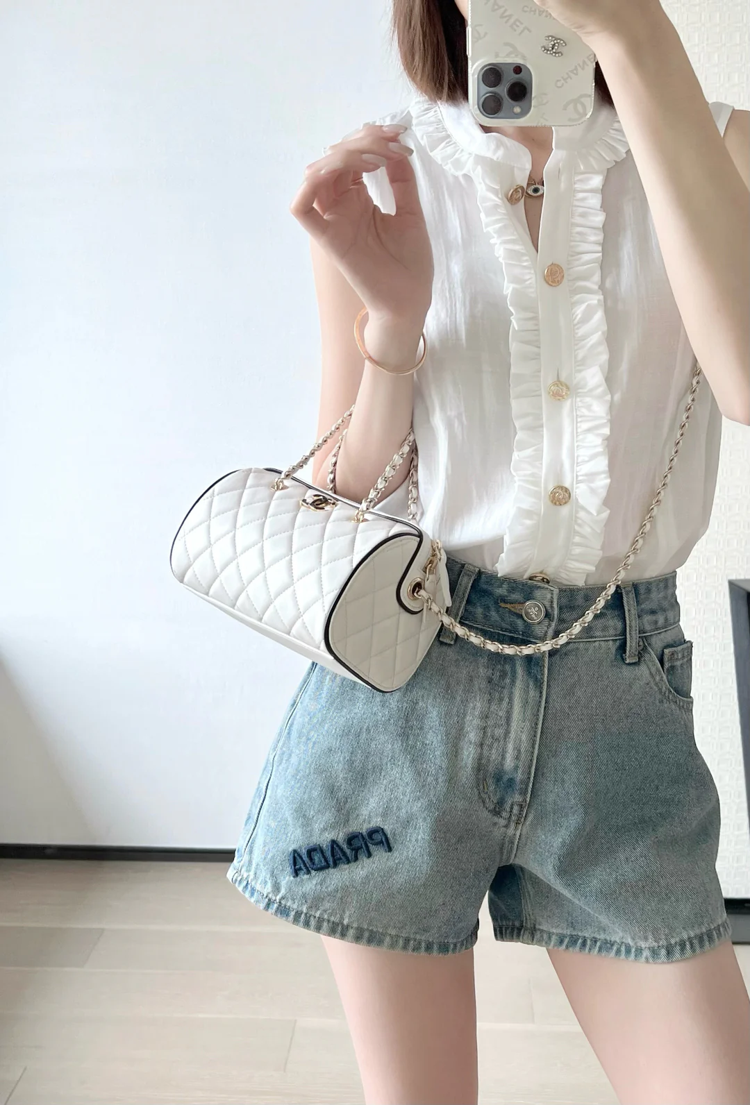 Мини-сумка-котелок Chanel 25p из овечьей кожи, белая с черной отделкой и светло-золотистой пряжкой.