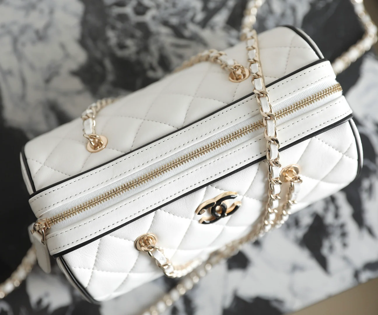 Мини-сумка-котелок Chanel 25p из овечьей кожи, белая с черной отделкой и светло-золотистой пряжкой.