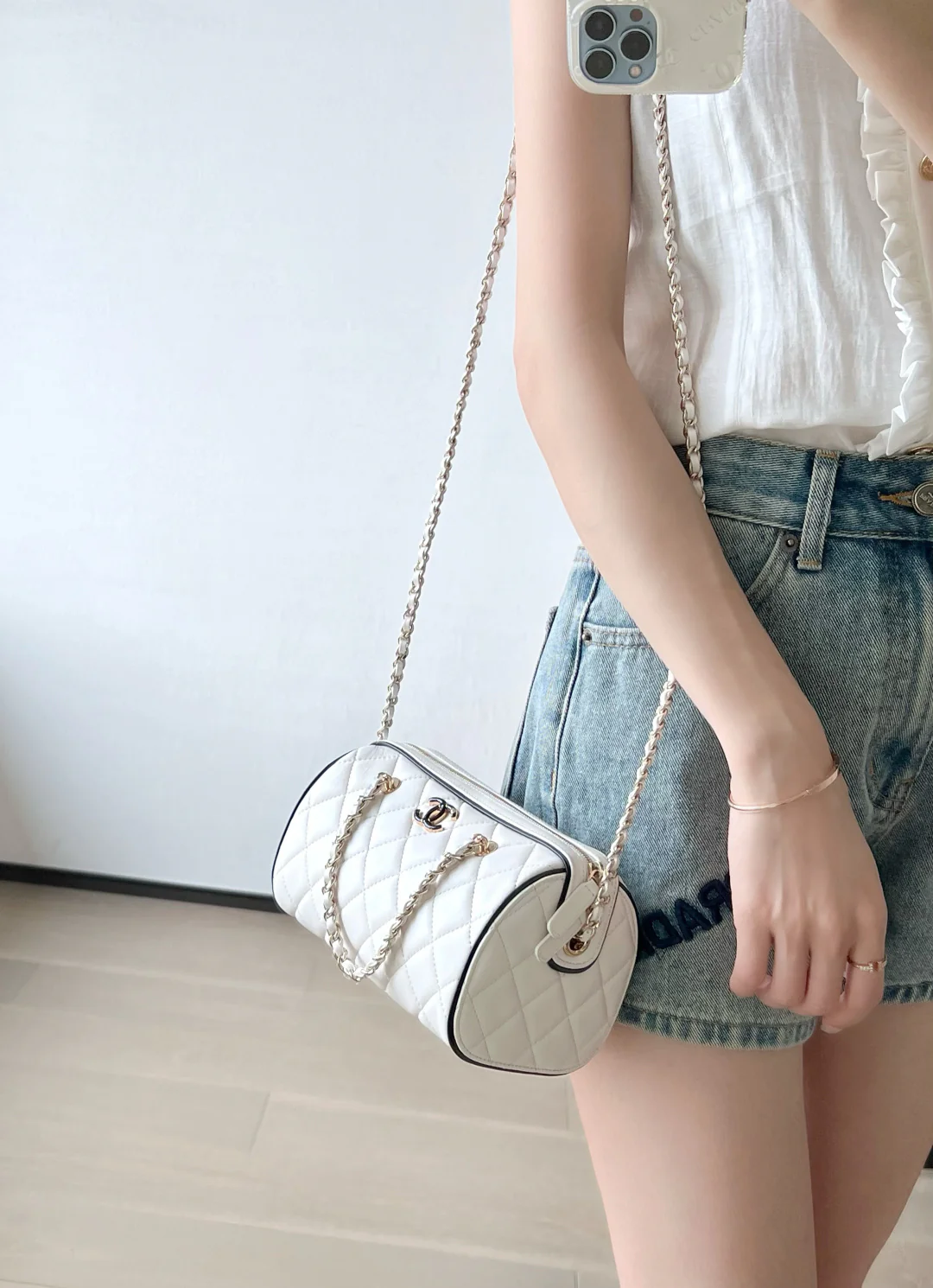 Мини-сумка-котелок Chanel 25p из овечьей кожи, белая с черной отделкой и светло-золотистой пряжкой.