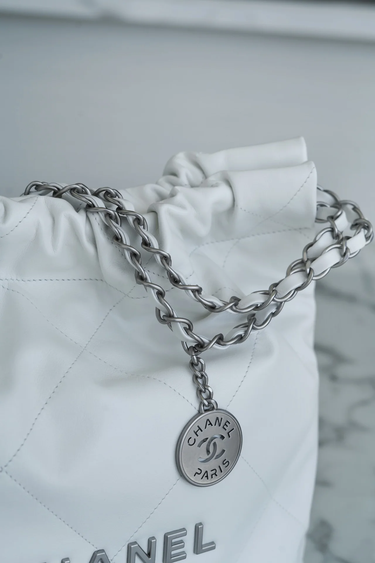 Сумочка Chanel No. 22 — маленькая, белая, серебристая.