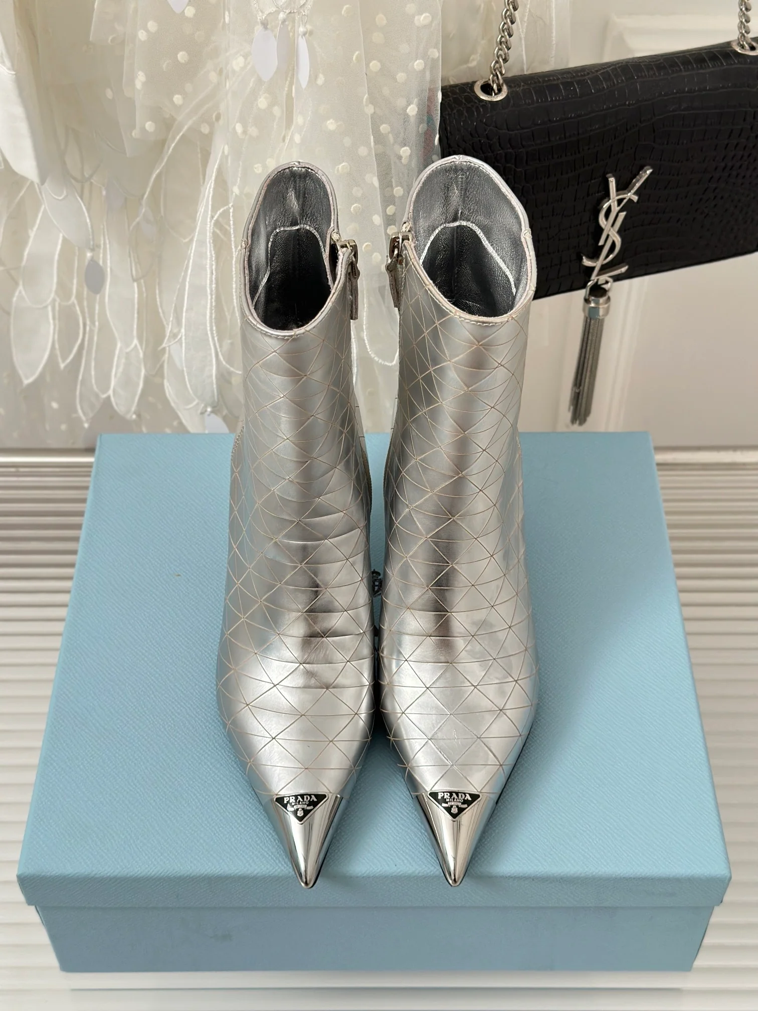 Новинка сезона осень/зима 2023 от Prada — ботильоны с острым носком и треугольным логотипом — серебристые.