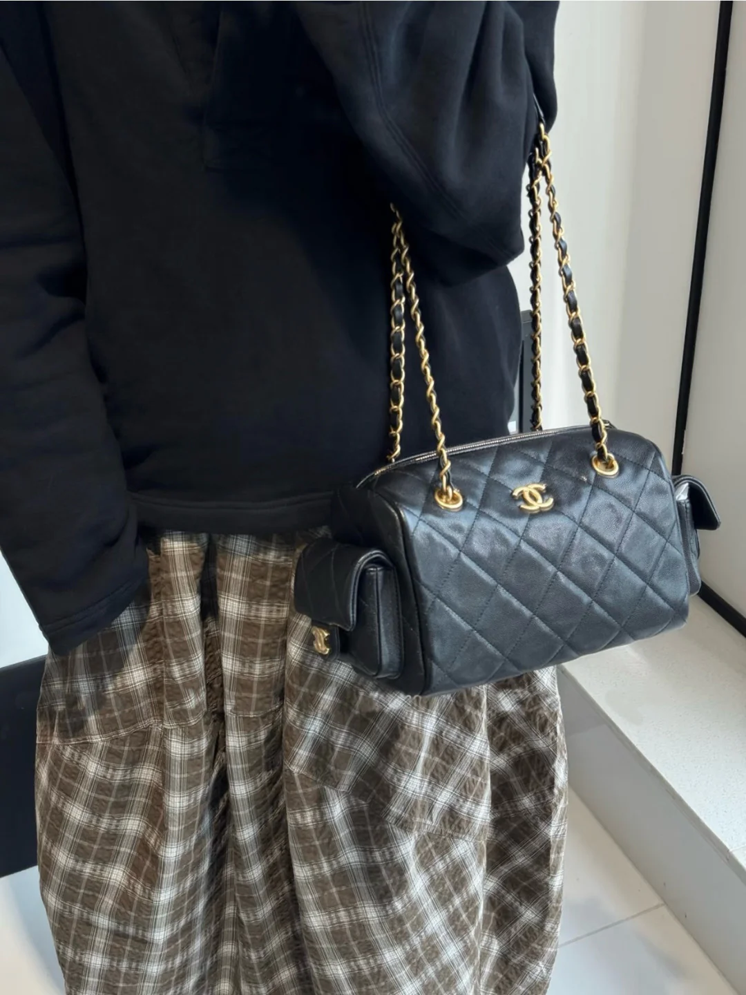 Сумка-боулинг Chanel 25k с двумя карманами — черная кожа с золотой пряжкой и маленьким шариком.