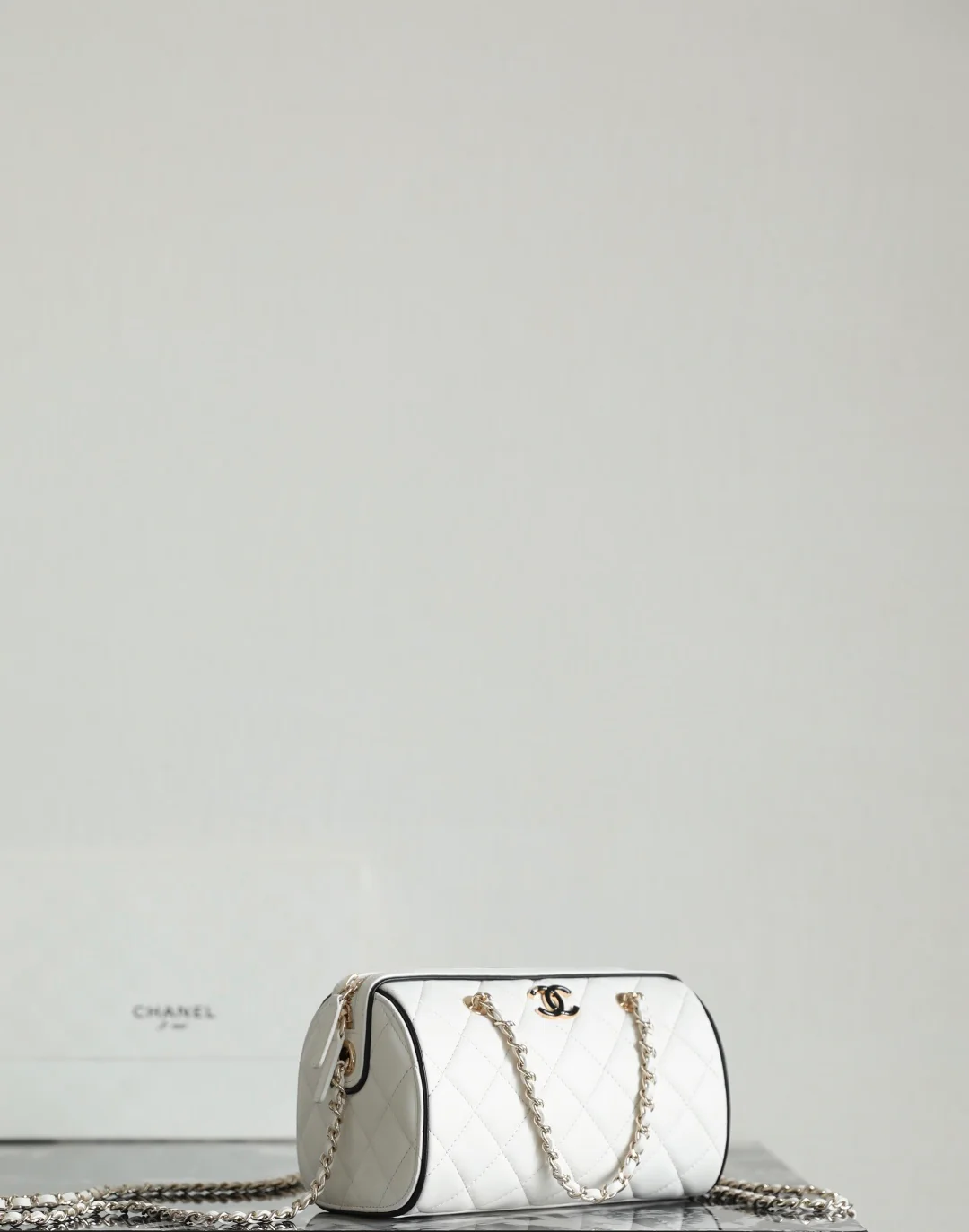 Мини-сумка-котелок Chanel 25p из овечьей кожи, белая с черной отделкой и светло-золотистой пряжкой.