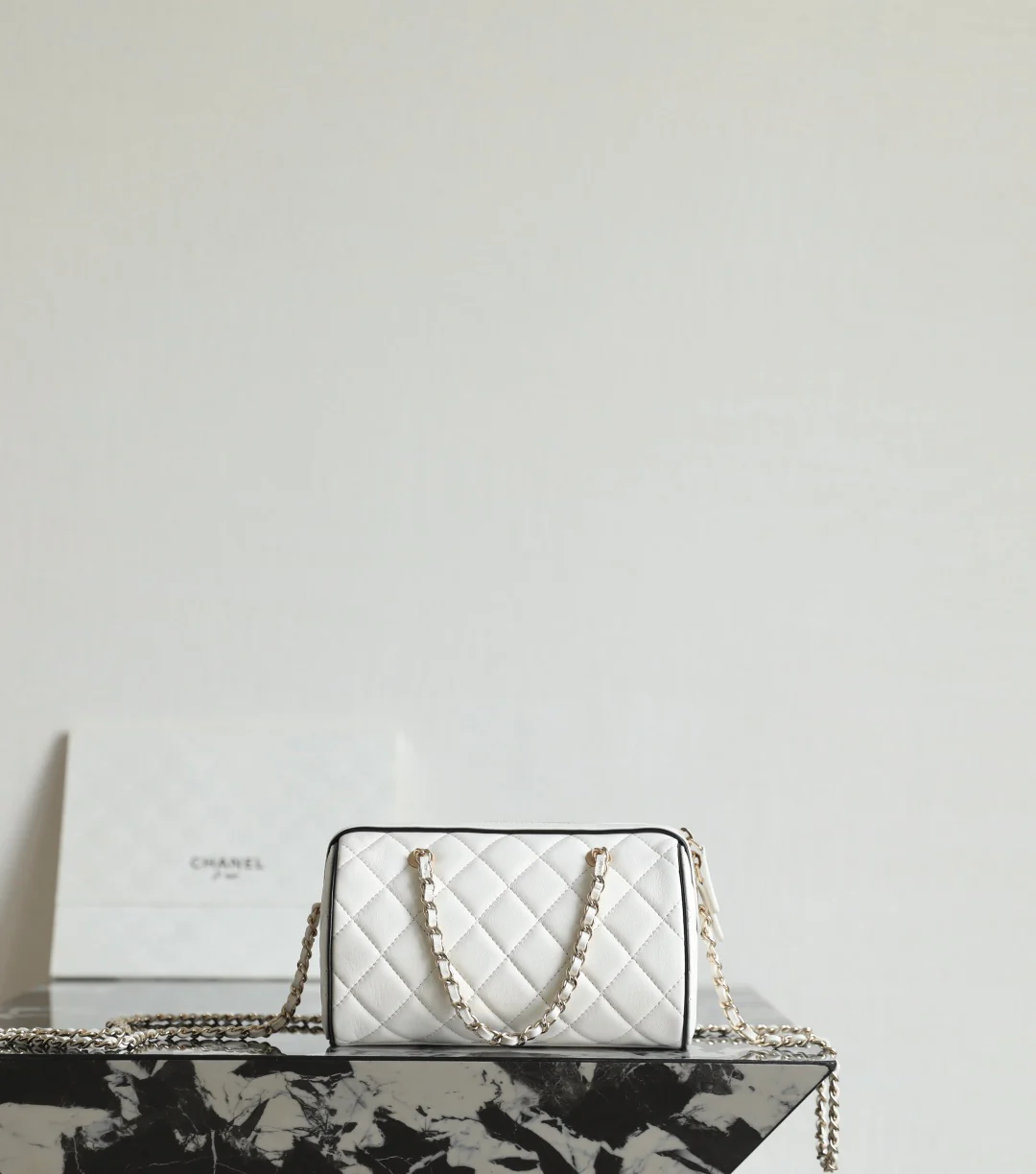 Мини-сумка-котелок Chanel 25p из овечьей кожи, белая с черной отделкой и светло-золотистой пряжкой.