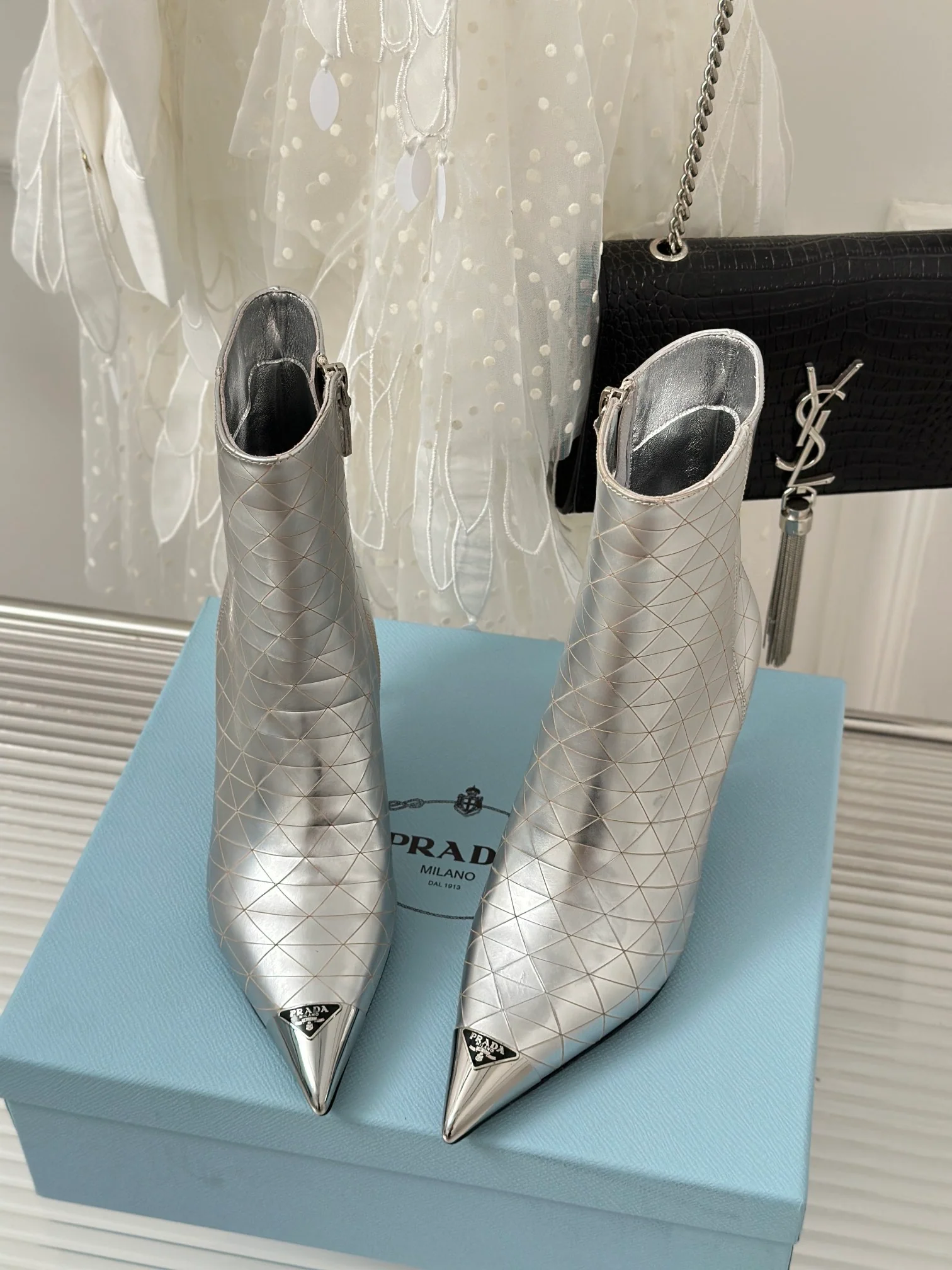 Новинка сезона осень/зима 2023 от Prada — ботильоны с острым носком и треугольным логотипом — серебристые.
